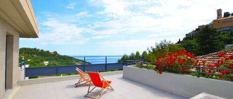 A terrace with a view of the sea, a red chair, and a wooden table.