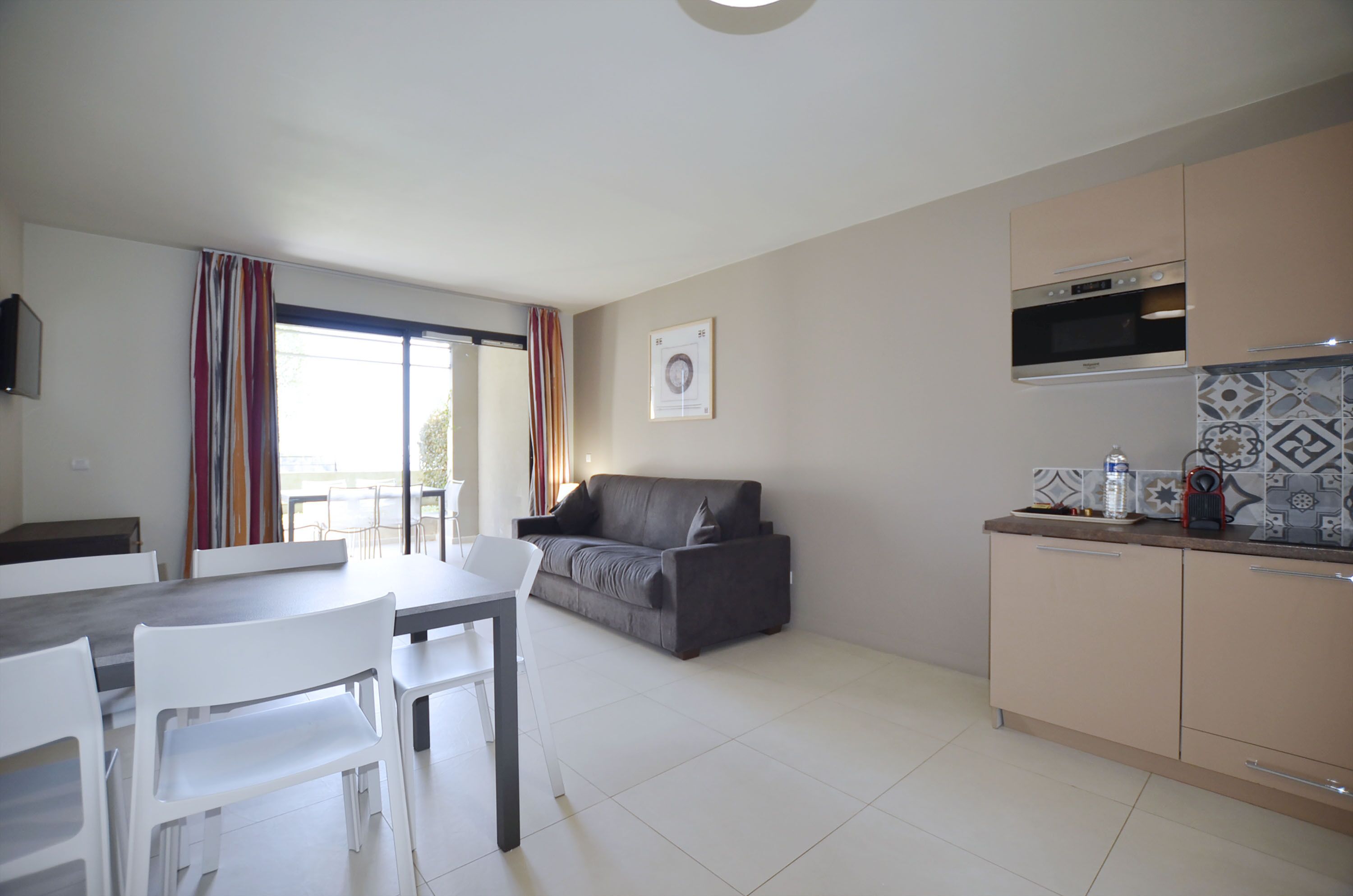 Un appartement moderne comprenant un coin repas, un canapé, une kitchenette et une grande fenêtre avec des rideaux.