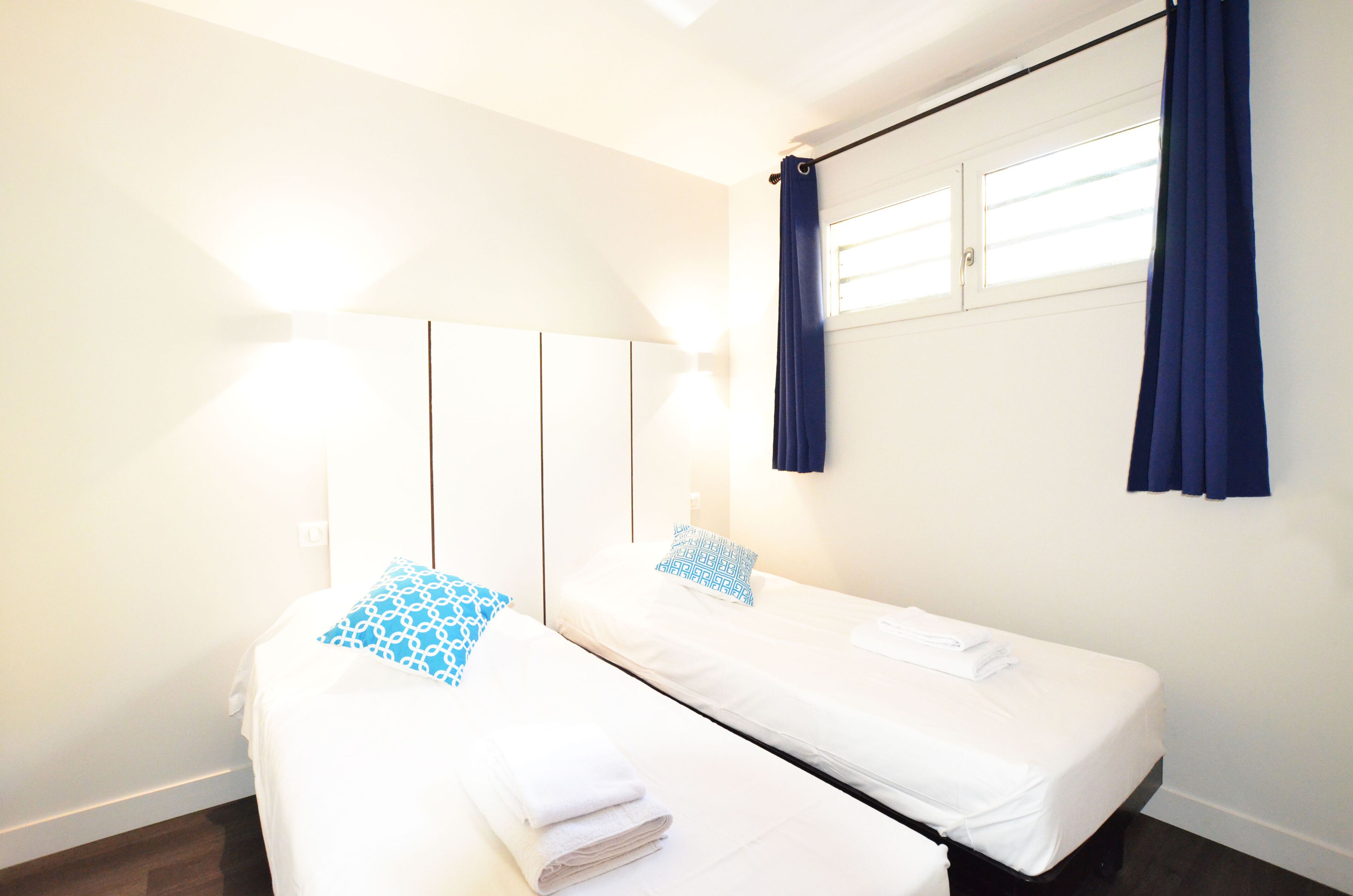 Ein Zimmer mit zwei Einzelbetten, einem großen Spiegel, einem Fenster mit Vorhängen und einer Wandleuchte.