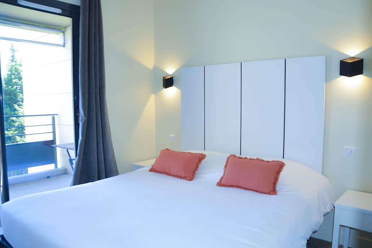 Habitación de hotel con una cama grande, dos almohadas, una mesita de noche y una lámpara fijada a la pared.