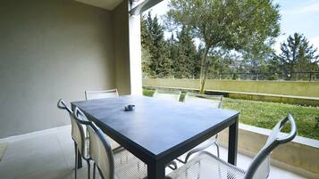 A balcony with a table and chairs, a view of trees and a fence, and a clear sky.