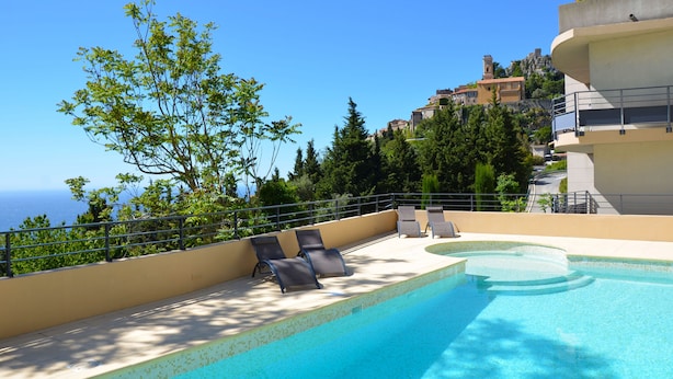 A rooftop pool with lounge chairs, a clear view of the sea, and buildings in the background.