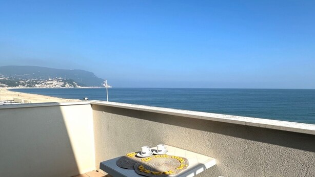 Un balcón con vista al mar, un par de zapatos y un sombrero sobre una estera.