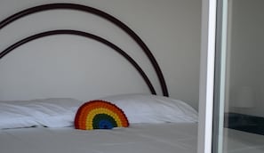 A bed with a white mattress and pillows, a rainbow-shaped pillow, and a wooden headboard.