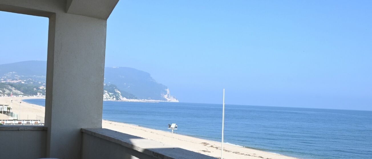 A beach view with a clear sky, a sandy shore, and a distant mountain.