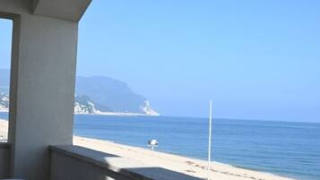 A beach view with a clear sky, a sandy shore, and a distant mountain.