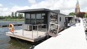 A modern floating houseboat docked at a pier with a church in the background.
