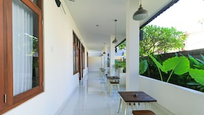 A corridor with tables and benches, large windows, and hanging lights. - Kak Garden Inn by Zuzu (Kuta)