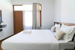 A hotel room with a large bed, a TV on the wall, and a window with curtains. - Kak Garden Inn by Zuzu (Kuta)