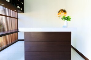 A reception desk with a modern design, a potted plant, and a wall-mounted light fixture. - Kak Garden Inn by Zuzu (Kuta)