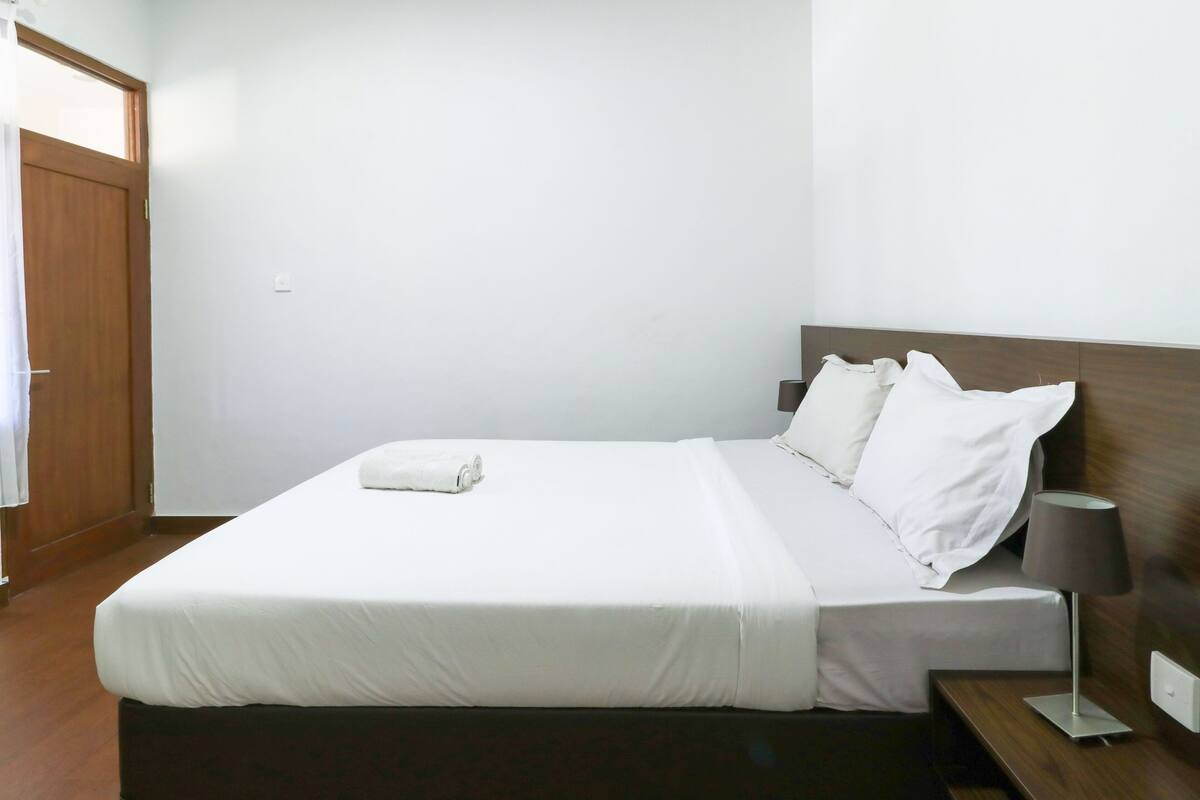 A neatly made bed with white linens, a wooden headboard, and a bedside table with a lamp.
