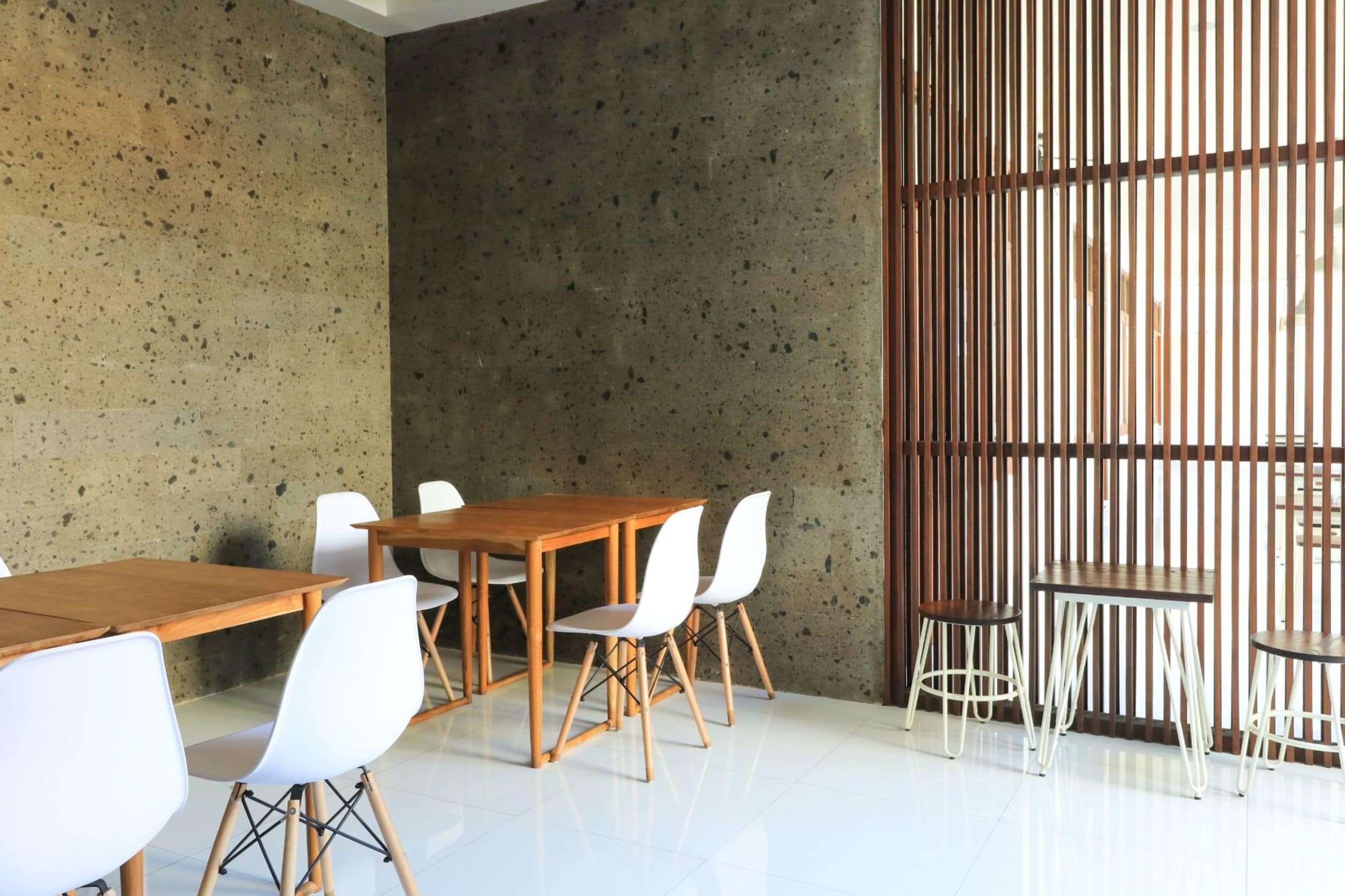 Una sala de reuniones moderna con pared de concreto, mesas de madera y sillas blancas.