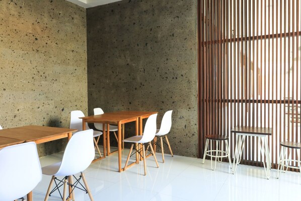 A modern meeting room with a concrete wall, wooden tables, and white chairs. - Kak Garden Inn by Zuzu (Kuta)