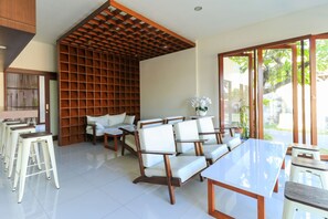 A modern interior with a dining area, seating, and a view through large glass doors. - Kak Garden Inn by Zuzu (Kuta)