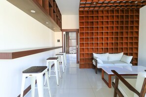 A modern hotel room with a sofa, a dining table, and two bar stools. - Kak Garden Inn by Zuzu (Kuta)