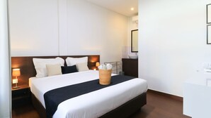 A hotel room with a large bed, a bedside table with a lamp, a small side table, and a mirror on the wall. - Kak Garden Inn by Zuzu (Kuta)
