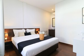 A hotel room with a large bed, a bedside table with a lamp, a small side table, and a mirror on the wall. - Kak Garden Inn by Zuzu (Kuta)