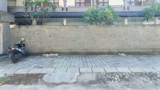 A paved area with a concrete wall, a parked motorcycle, and some plants. - Kak Garden Inn by Zuzu (Kuta)