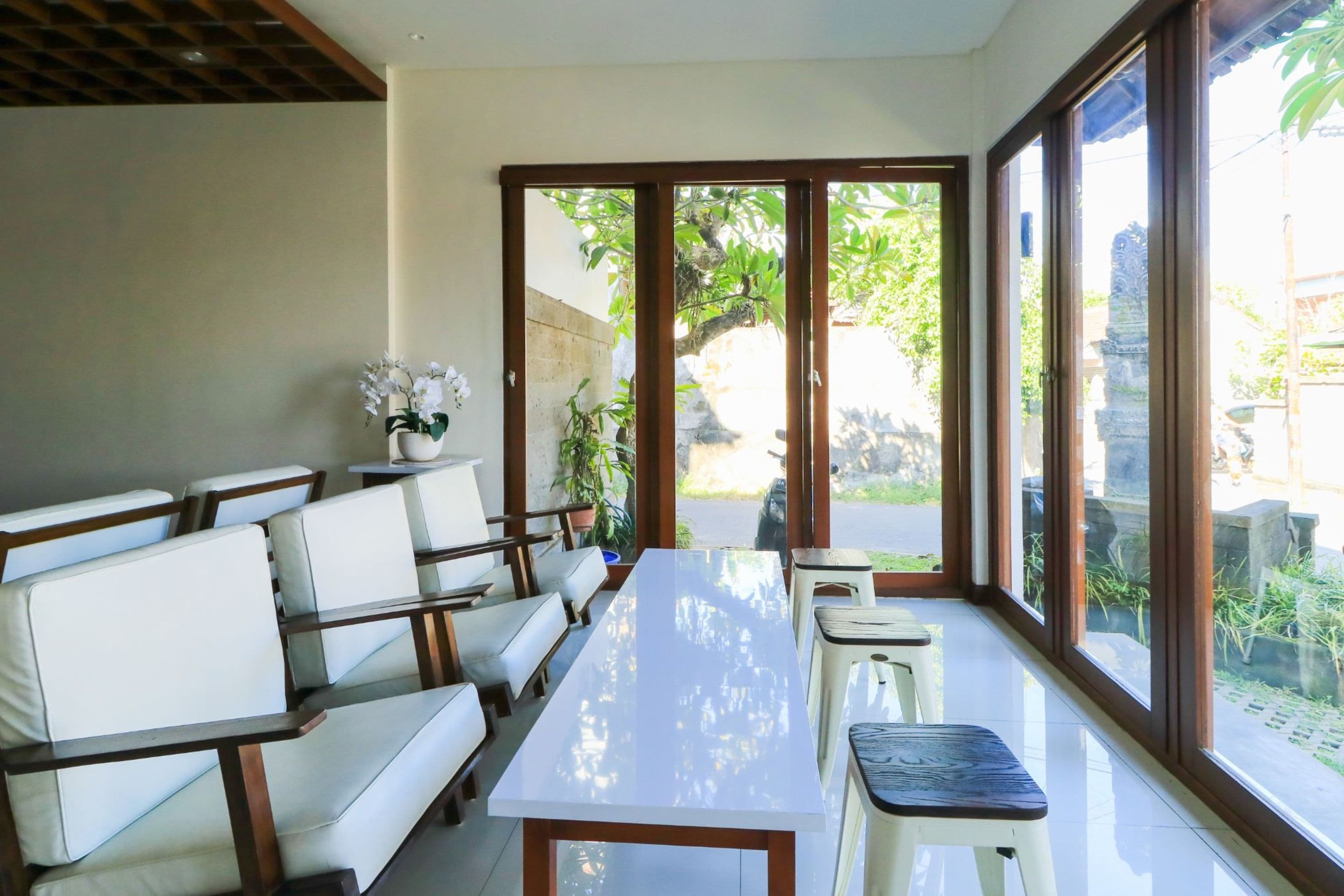 A modern dining area with a long table, white cushioned seating, and large windows offering a view of the outdoors.