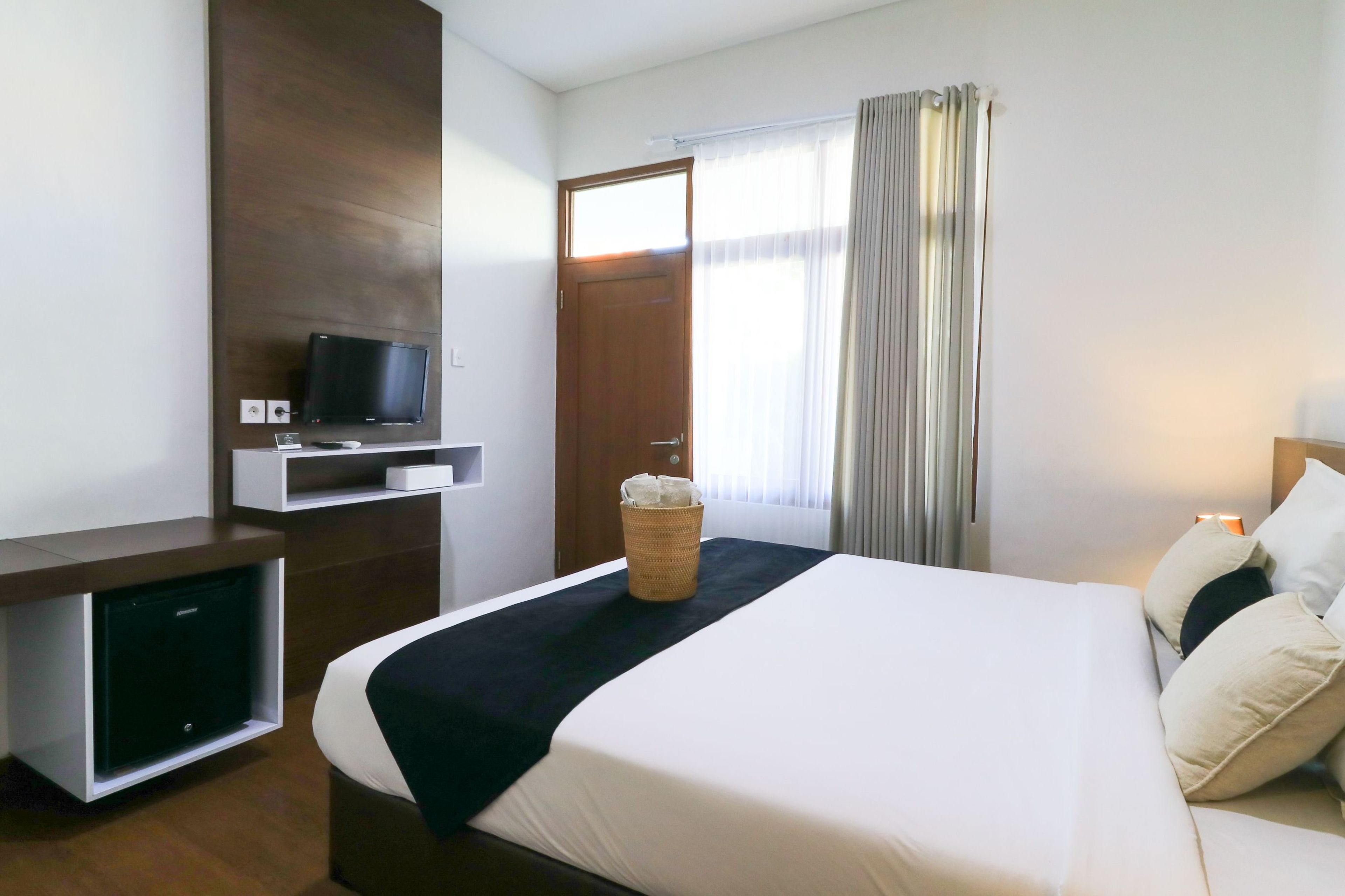 Una habitación de hotel con una cama, un televisor en un mueble bajo, un escritorio pequeño y una ventana con cortinas.