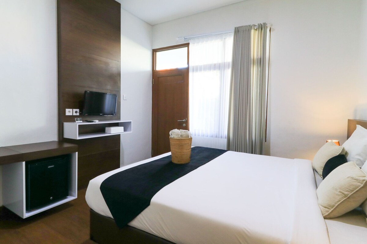 Una habitación de hotel con una cama, un televisor en un mueble bajo, un escritorio pequeño y una ventana con cortinas.