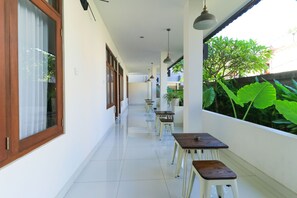 A corridor with tables and benches, large windows, and hanging lights. - Kak Garden Inn by Zuzu (Kuta)