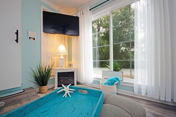 A room with a large window, a fireplace, a blue pool table, and a cozy seating area.