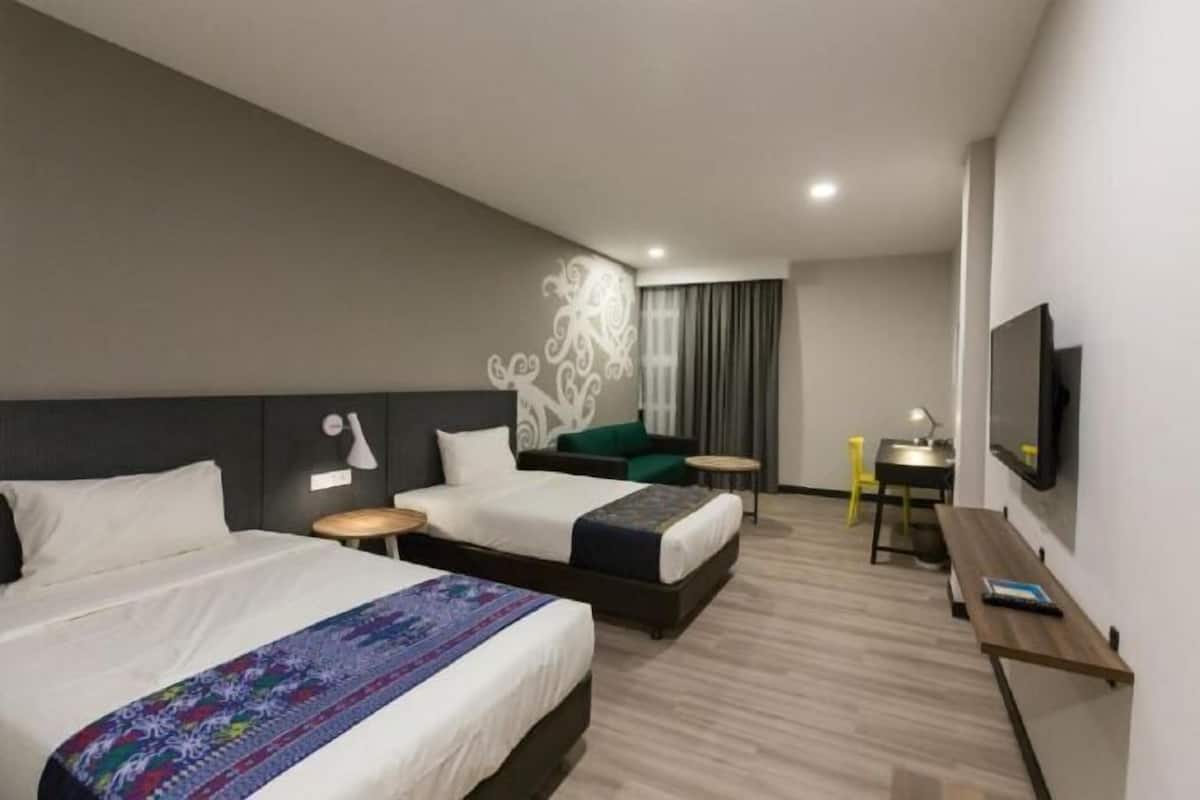 Habitación de hotel con dos camas, un escritorio, una silla, un televisor y un elemento decorativo en la pared.