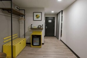 Un pasillo con un banco, una mesita con hervidor y una puerta al final.