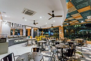 Ein Restaurant mit mehreren Tischen, Stühlen, Deckenventilatoren und einer Bar.