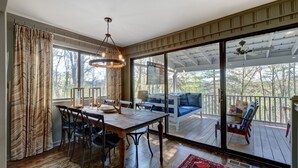Un espace repas comprenant une table et des chaises en bois, un lustre et une vue sur une terrasse aménagée avec des sièges d’extérieur.