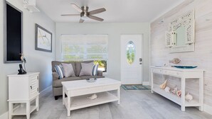 A room with a ceiling fan, a sofa with cushions, a coffee table, a white console table with decorative items, and a door with a glass panel. - Waterfront, oceanview renovated pvt. 3 bedroom, 3.5 bath with pool and dockage. (Marathon)