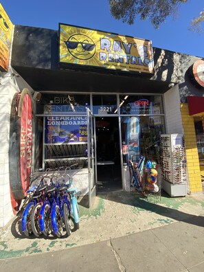 Een winkelgefaciliteit met een bordje dat 'Ray's Rentals' zegt, dat fietsen, surfplanken, skates, strandkleding en reparatieservices aanbiedt.