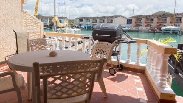 Un balcón con mesa y sillas, con vista a un puerto deportivo con barcos y edificios.