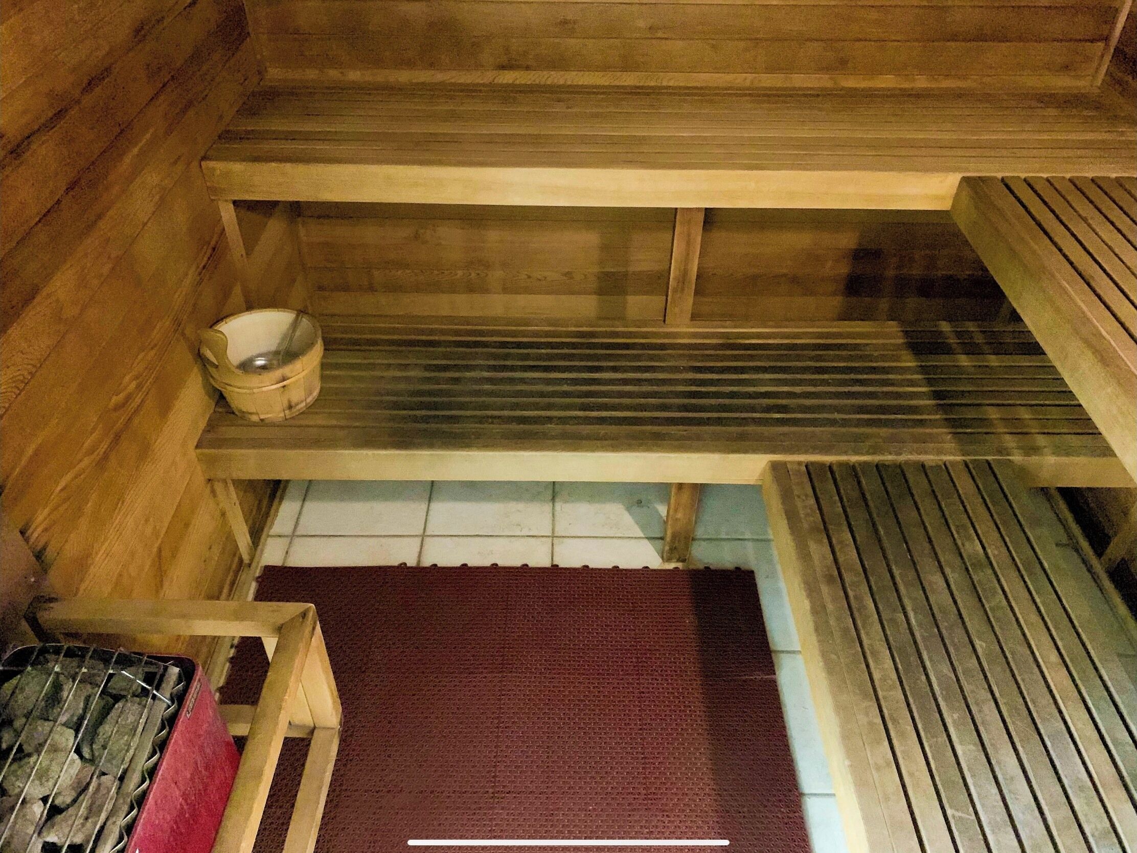 Un sauna en bois avec des bancs, une petite table en bois et un récipient en métal.