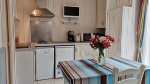 A compact kitchen with a microwave, toaster, and coffee maker. There is a dining table with a striped tablecloth and a vase of flowers. - Cottage Les Roses de mer ( Les Agapanthes ) (Sainte Marie de Ré)
