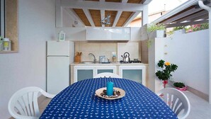 A compact kitchen with white cabinets, a sink, and a stove. There is a dining table with a blue tablecloth and a plate of food. - (MP63) Modern accommodation 150 mt from the sea (Marina Di Modica)