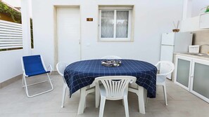 Et lille, rent værelse med et spisebord dækket til to personer, hvide stole, en blå stol, et køleskab og et vindue med et matteret glasdesign.