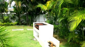 Un espace extérieur aménagé avec des sièges blancs, comprenant un banc et une table, entouré de palmiers luxuriants et d’une pelouse verdoyante.