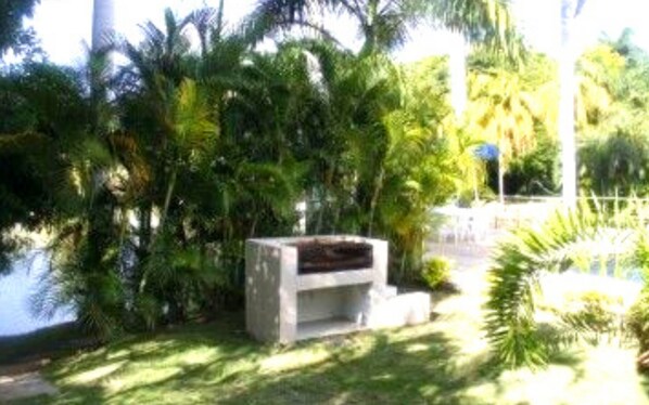 Un área jardín con una estructura de concreto, posiblemente un espacio de descanso, rodeada de diversos tipos de follaje y árboles.