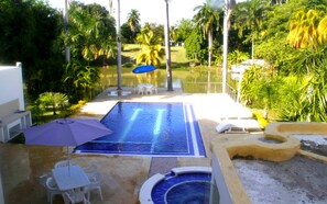 Una piscina con fuente de agua azul, rodeada de palmeras y césped.