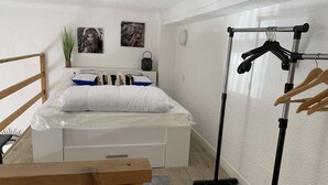 Een slaapkamer met een bed, een houten bankje, een kledingrek en twee foto’s aan de muur.