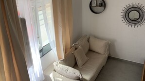 Een kamer met een beige bank, een radiator en een ronde spiegel aan de muur.