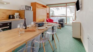 A modern kitchen with a wooden table, clear chairs, and a red chair. A microwave and coffee maker are on the counter.