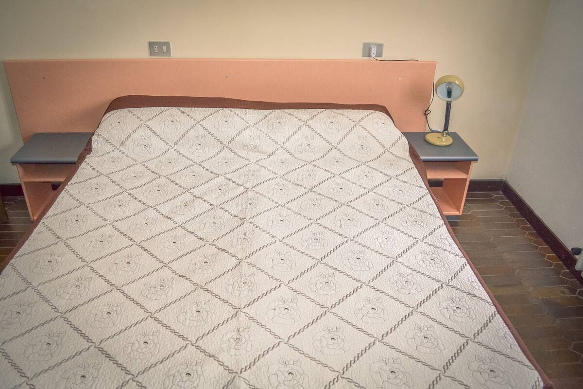 A bed with a quilted headboard and footboard, two bedside tables, and a nightstand with a lamp.
