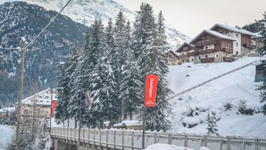A snow-covered mountain area with a wooden bridge, a ski lift, and buildings with balconies. - Hotel Milano (Valfurva)