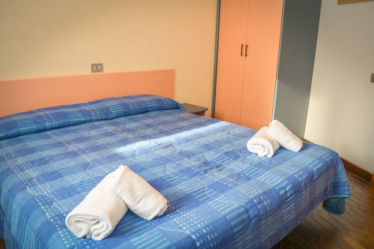 A neatly made bed with a blue patterned bedspread and two rolled white towels.