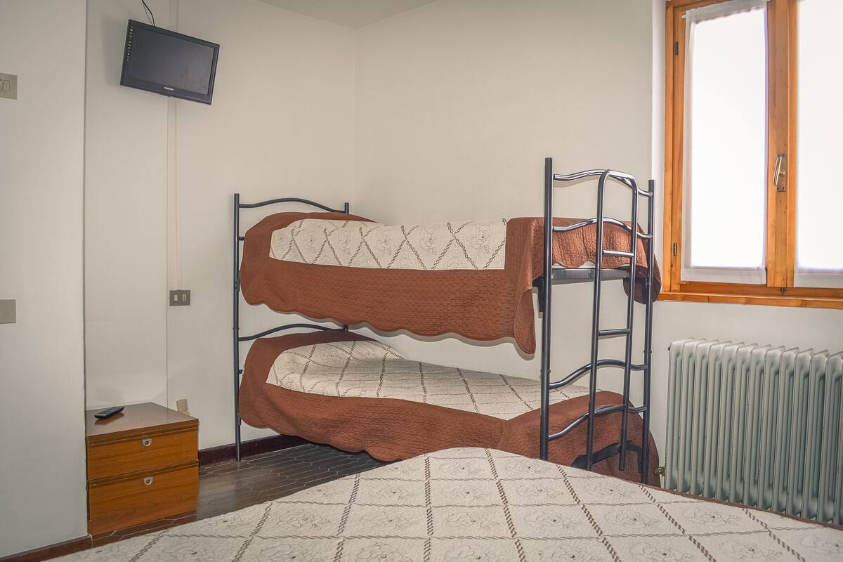 A bunk bed with a ladder, a wooden dresser, a radiator, and a television on the wall.