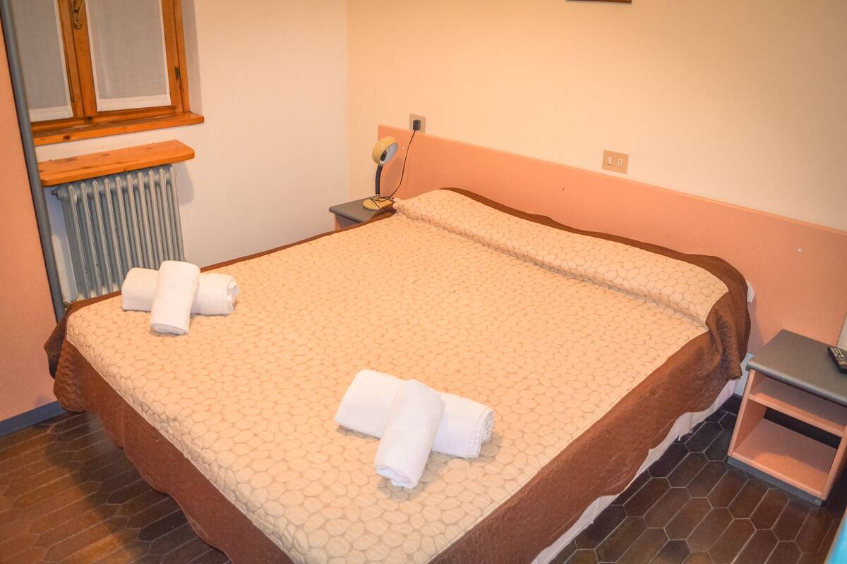 A neatly made bed with a patterned bedspread and two rolled towels on the side.