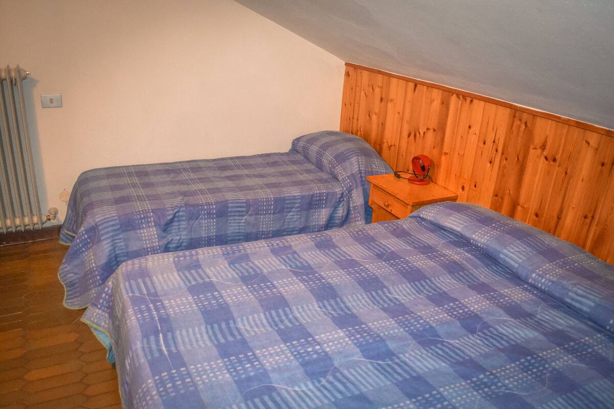 A room with two beds, wooden panel walls, a radiator, and a wooden nightstand.